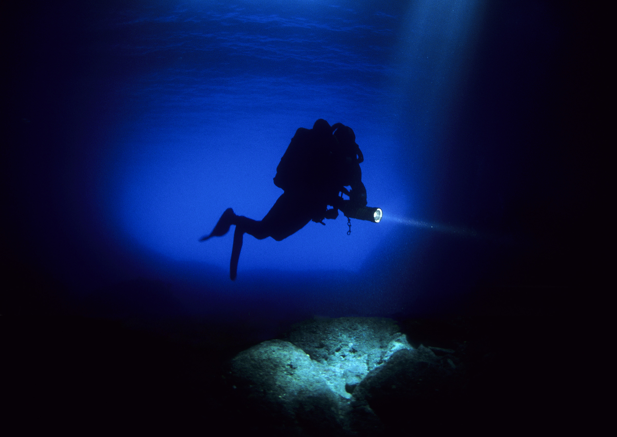 Diver lit by blue water in a cave-like passage near Vis